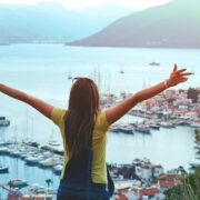 Woman raising her hands in the air looking out at a view of boats